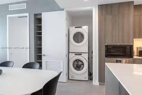 Built-in laundry closet with stacked washer and dryer, adjacent custom shelving, and modern cabinetry featuring a built-in microwave