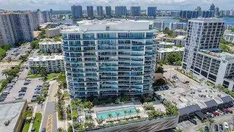 High-rise residential building featuring floor-to-ceiling glass paneling, a multi-level concrete facade, and an elevated outdoor swimming pool with mature palms