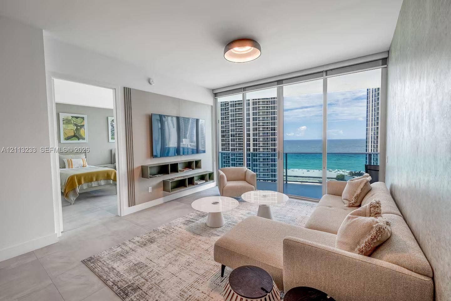 Living space featuring floor-to-ceiling glass sliding doors, custom wall-mounted media shelving, recessed ceiling lighting, and large-format tile flooring