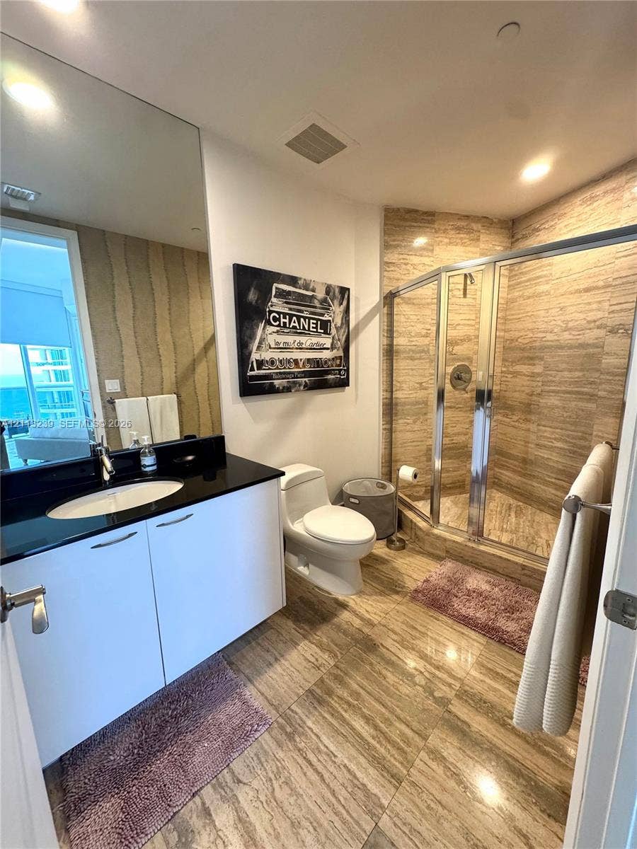 16001 Collins Avenue, #2403, Sunny Isles Beach, Sunny Isles Beach, FL 33160 Full-height vanity mirror, dark stone-surface countertop, white cabinetry, walk-in shower with stone tile surround, and large-format stone floor tile