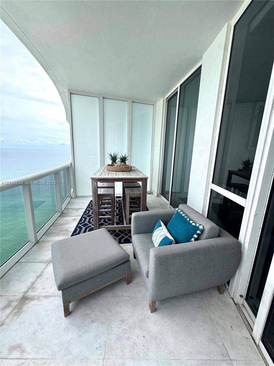 16001 Collins Avenue, #2403, Sunny Isles Beach, Sunny Isles Beach, FL 33160 Covered balcony featuring large-format stone tile flooring, a glass panel railing, and expansive floor-to-ceiling glass sliding doors