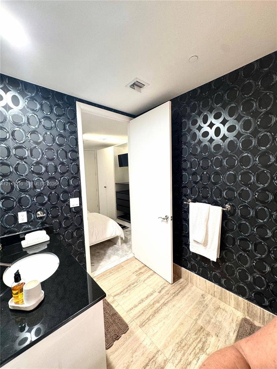16001 Collins Avenue, #2403, Sunny Isles Beach, Sunny Isles Beach, FL 33160 Bathroom featuring high-contrast geometric patterned wall covering, stone-finish floor tile, and a black countertop vanity with a white drop-in basin