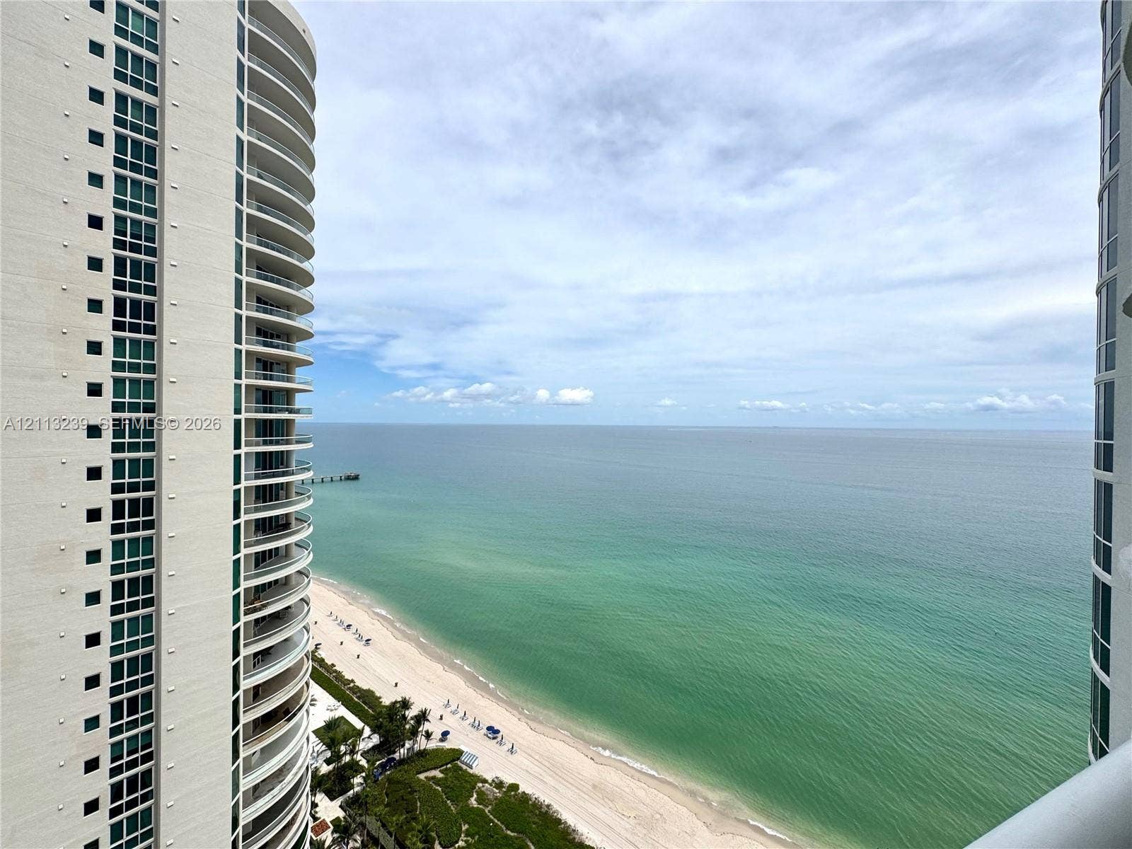 16001 Collins Avenue, #2403, Sunny Isles Beach, Sunny Isles Beach, FL 33160 High-rise balconies with glass railings overlooking a coastal shoreline and ocean expanse