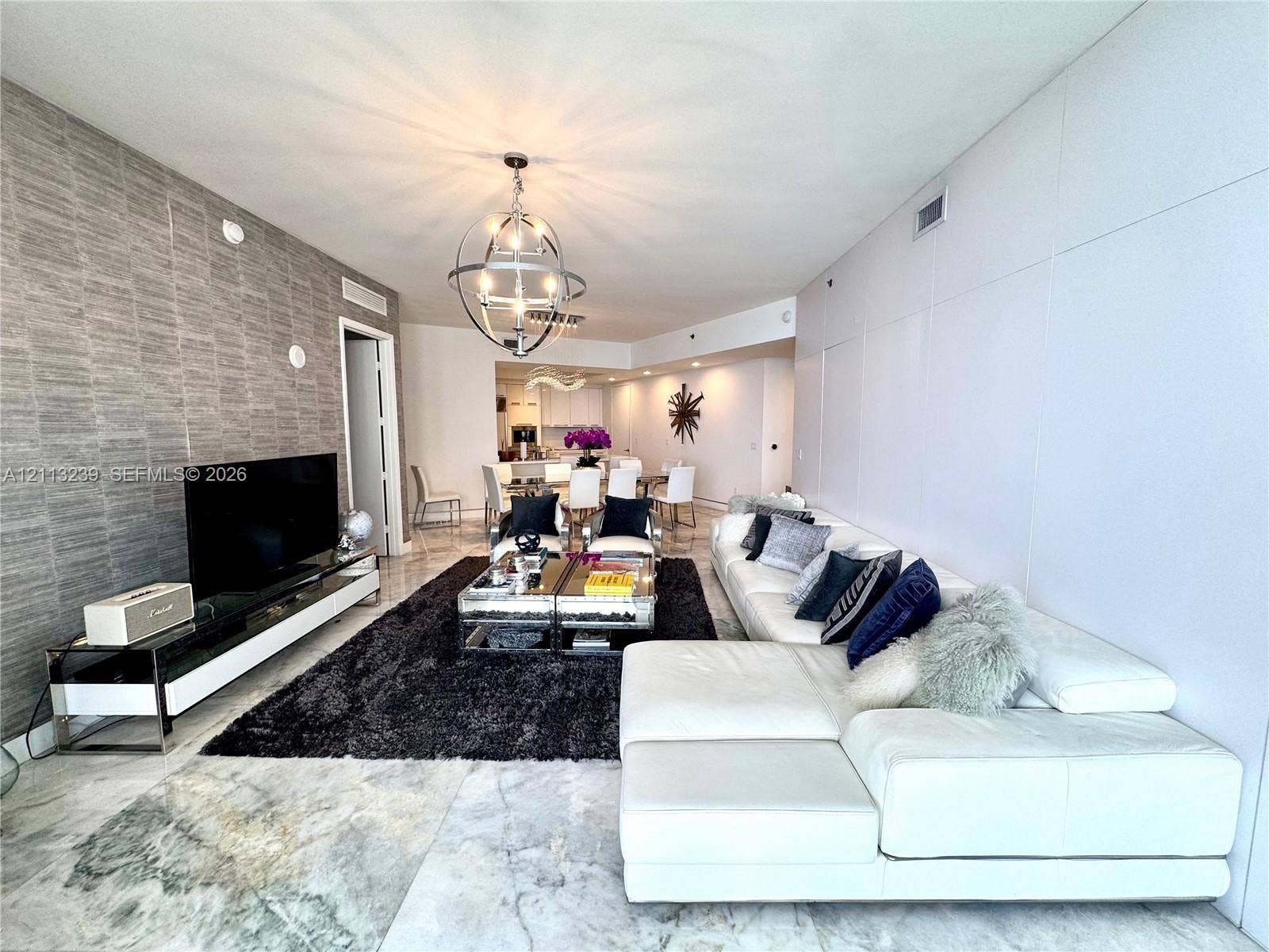 16001 Collins Avenue, #2403, Sunny Isles Beach, Sunny Isles Beach, FL 33160 Living space featuring polished stone flooring, textured accent wall, and a spherical multi-light chandelier