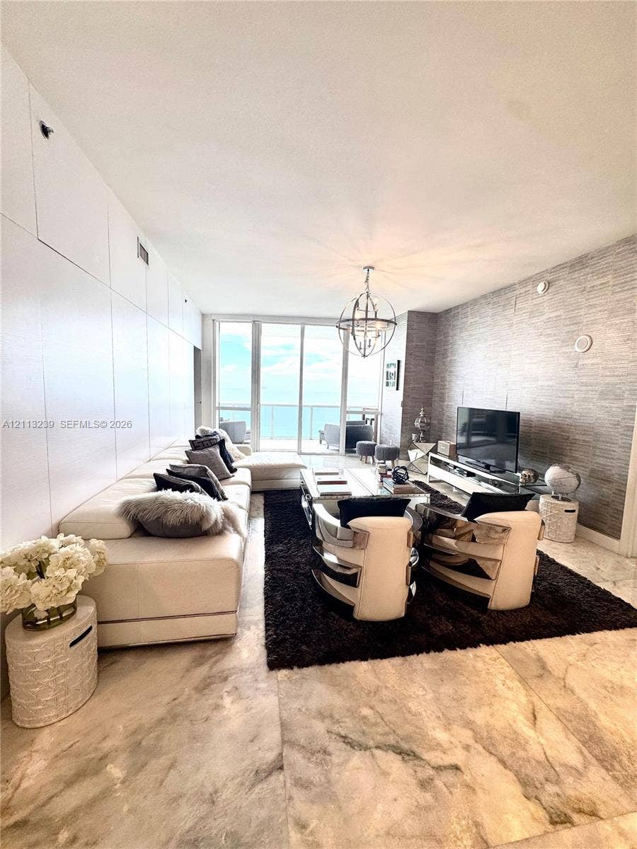 16001 Collins Avenue, #2403, Sunny Isles Beach, Sunny Isles Beach, FL 33160 Living area featuring floor-to-ceiling glass paneling, stone tile flooring, a textured feature wall, and a contemporary spherical pendant light fixture