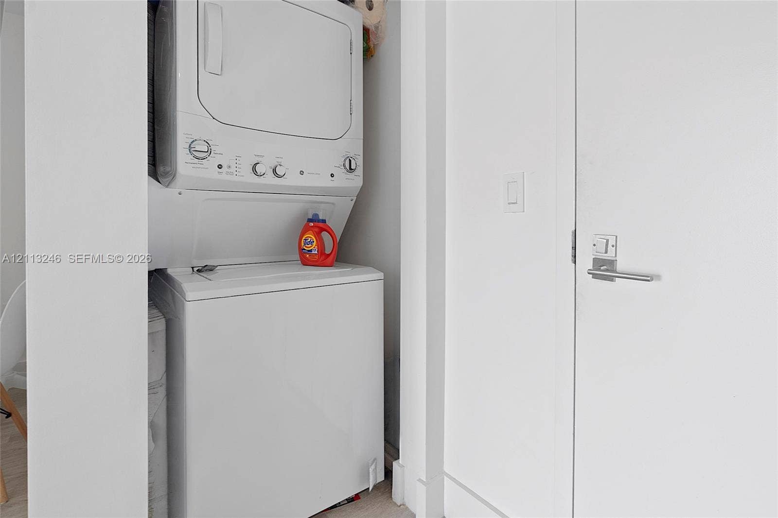 121 NE 34th Street, #2703, Miami, FL 33137 Stacked white washer and dryer unit housed within a dedicated laundry alcove featuring a swing door with a modern satin nickel lever handle