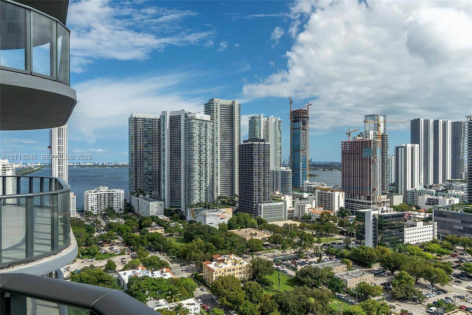121 NE 34th Street, #2703, Miami, FL 33137 Curved balcony with glass and metal railings, overlooking an urban skyline and coastal waterway