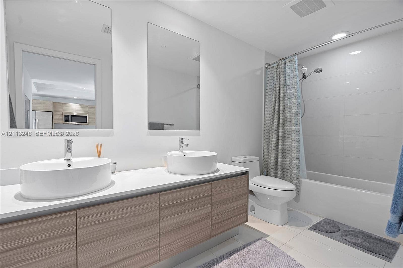 121 NE 34th Street, #2703, Miami, FL 33137 Floating wood-finish vanity with dual vessel sinks, white countertop, and frameless rectangular mirrors, accompanied by a combined soaking tub and shower with tile surround