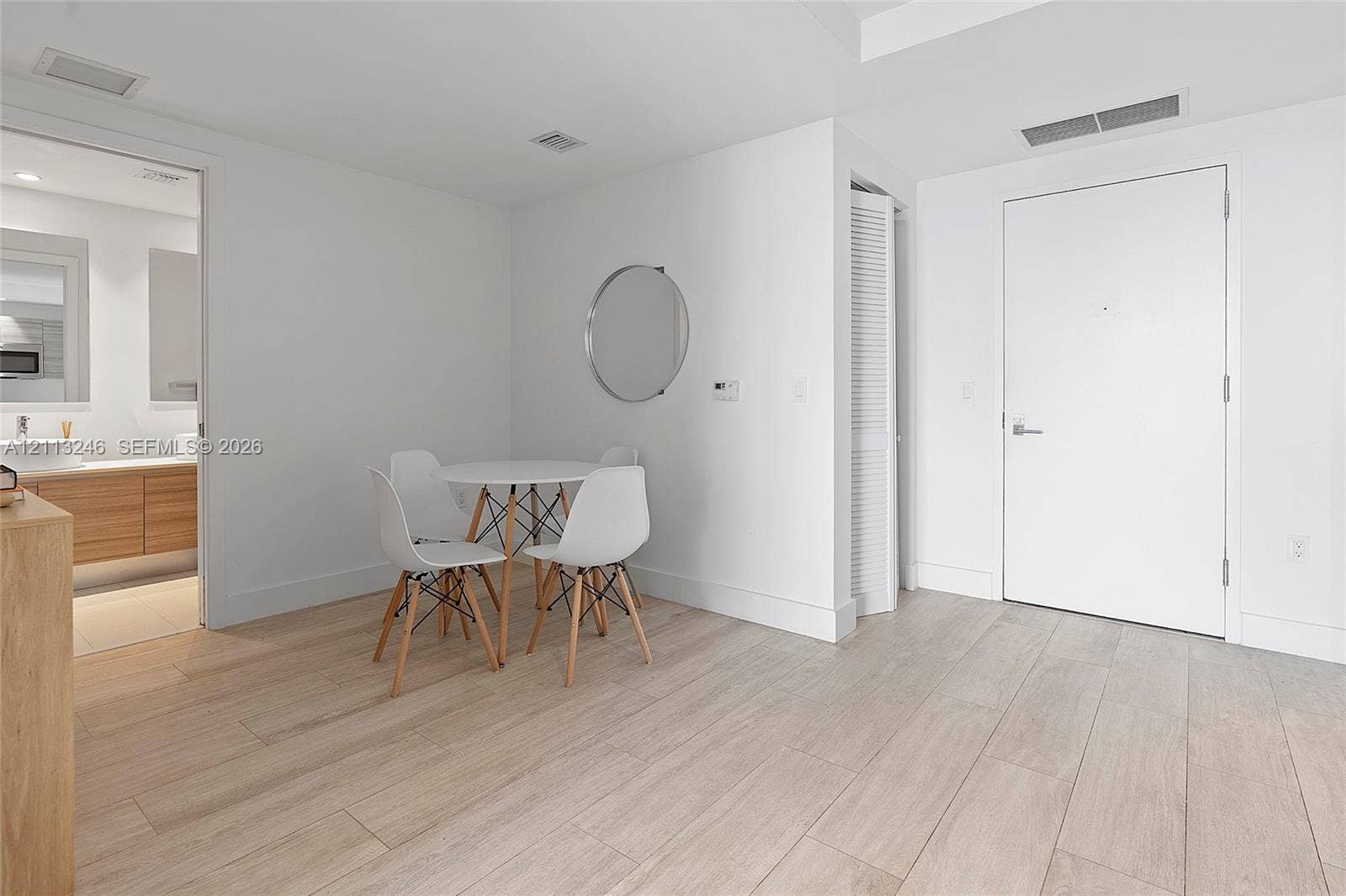 121 NE 34th Street, #2703, Miami, FL 33137 Open-concept area featuring light-toned wood-finish flooring, a wall-mounted circular mirror, and a bi-fold closet door