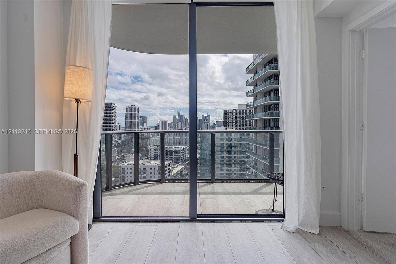 121 NE 34th Street, #2703, Miami, FL 33137 Floor-to-ceiling sliding glass door, private balcony with metal and glass railing, wood-finish flooring, and expansive urban skyline backdrop