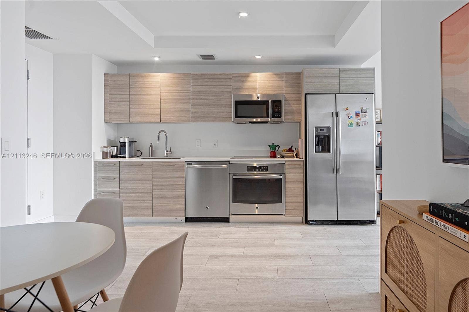 121 NE 34th Street, #2703, Miami, FL 33137 Kitchen featuring light wood-finish cabinetry, stainless steel appliances, a recessed tray ceiling, and stone-finish tile flooring