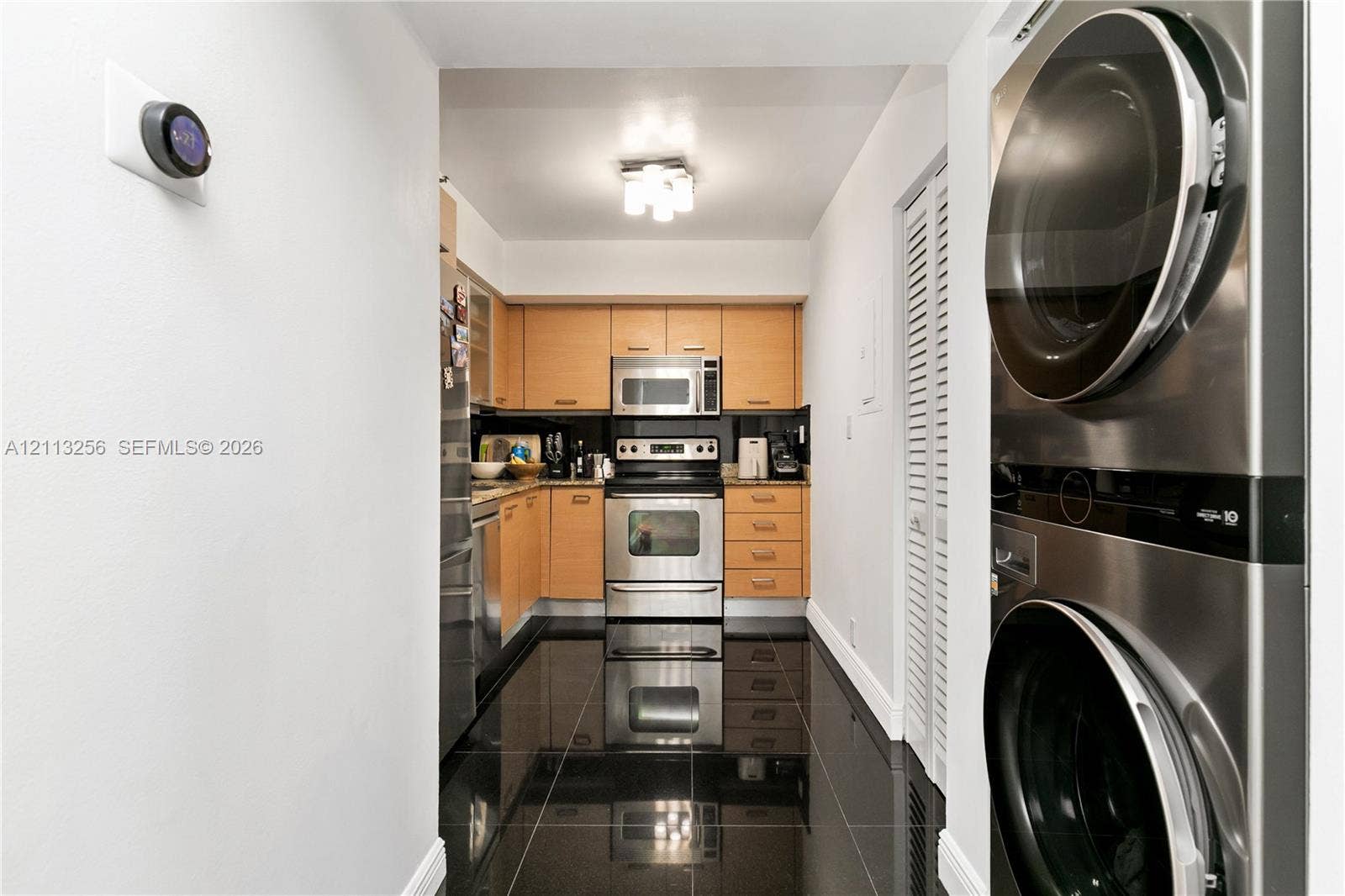 3300 NE 191st Street, #1514, Aventura, FL 33180 Kitchen featuring wood-finish cabinetry, stainless steel appliances, dark tile flooring, and a stacked laundry unit with louvered closet doors