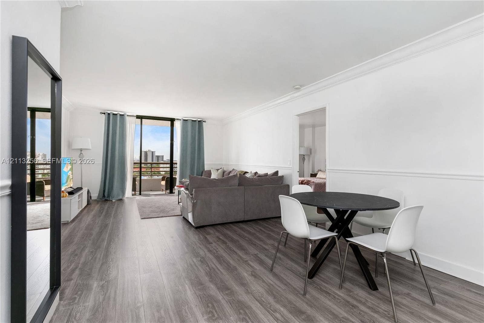 3300 NE 191st Street, #1514, Aventura, FL 33180 Open-concept living space featuring wood-finish flooring, crown molding, chair rail trim, and glass sliding doors providing exterior balcony access