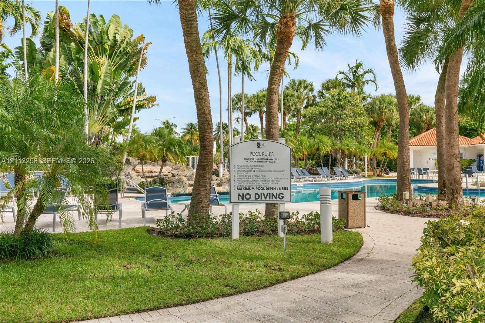 3300 NE 191st Street, #1514, Aventura, FL 33180 Swimming pool featuring a rock waterfall, surrounded by concrete paver decking, professional landscaping, and palm trees