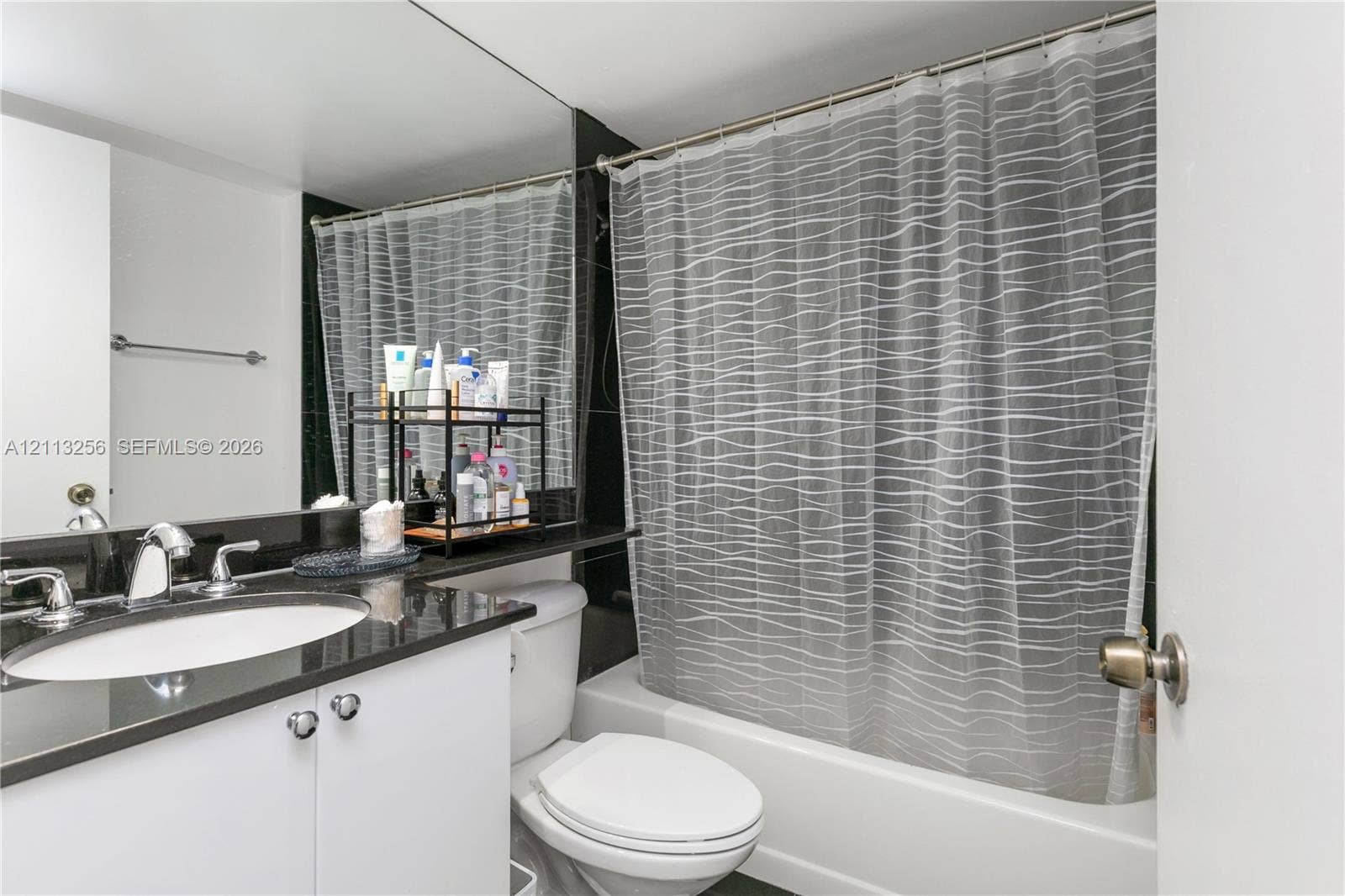 3300 NE 191st Street, #1514, Aventura, FL 33180 Bathroom featuring a vanity with dark stone countertop, integrated sink, polished chrome faucet, full-width mirror, and a built-in shower and tub combination.