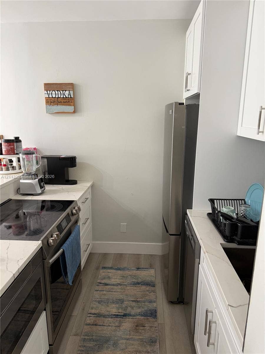 Kitchen featuring white cabinetry, quartz-style countertops, stainless steel appliances, and wood-finish flooring