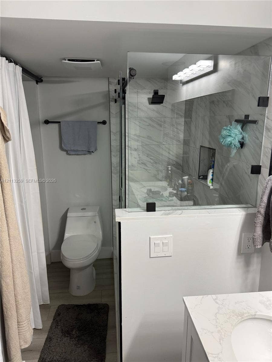 Bathroom featuring a walk-in shower with large-format stone-patterned tile, frameless glass enclosure, and matte black fixtures, paired with a vanity featuring a quartz countertop
