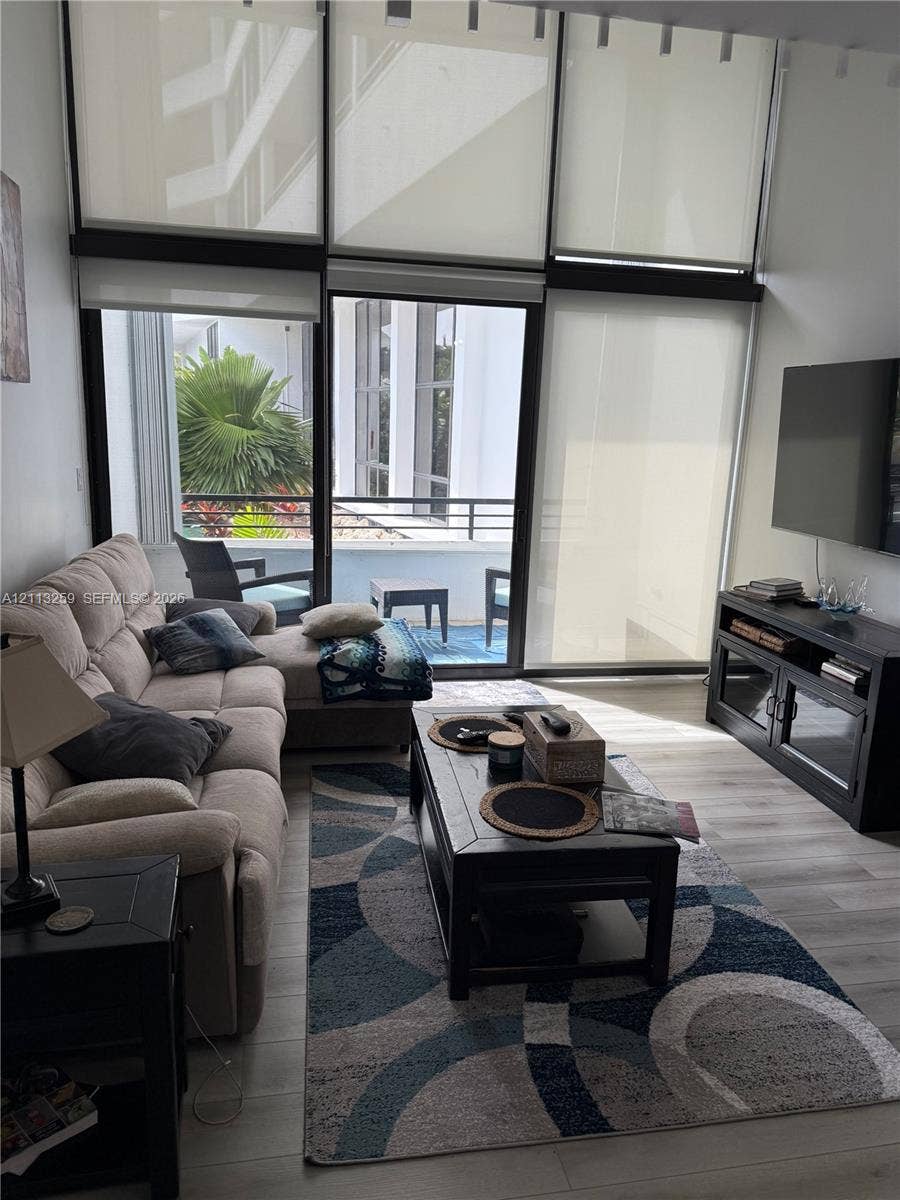 Floor-to-ceiling windows with roller shades, wood-finish flooring, and sliding glass door opening to a private balcony