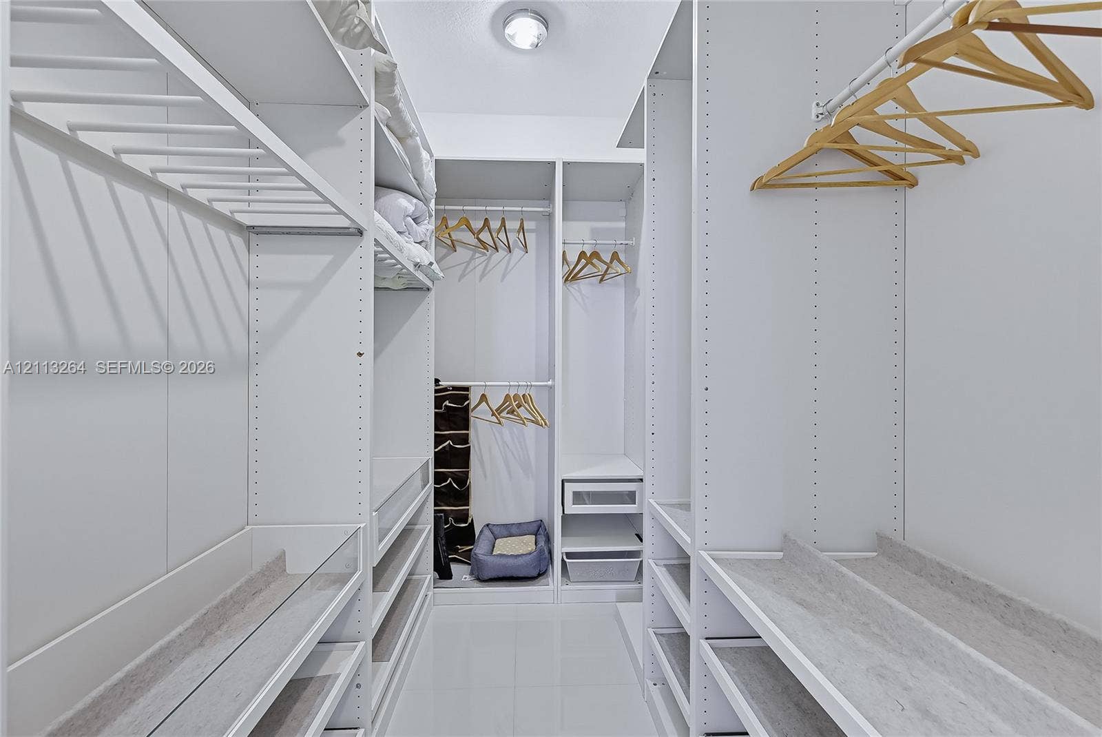 Walk-in closet featuring floor-to-ceiling white built-in shelving, adjustable storage racks, integrated hanging rods, and glossy tile flooring