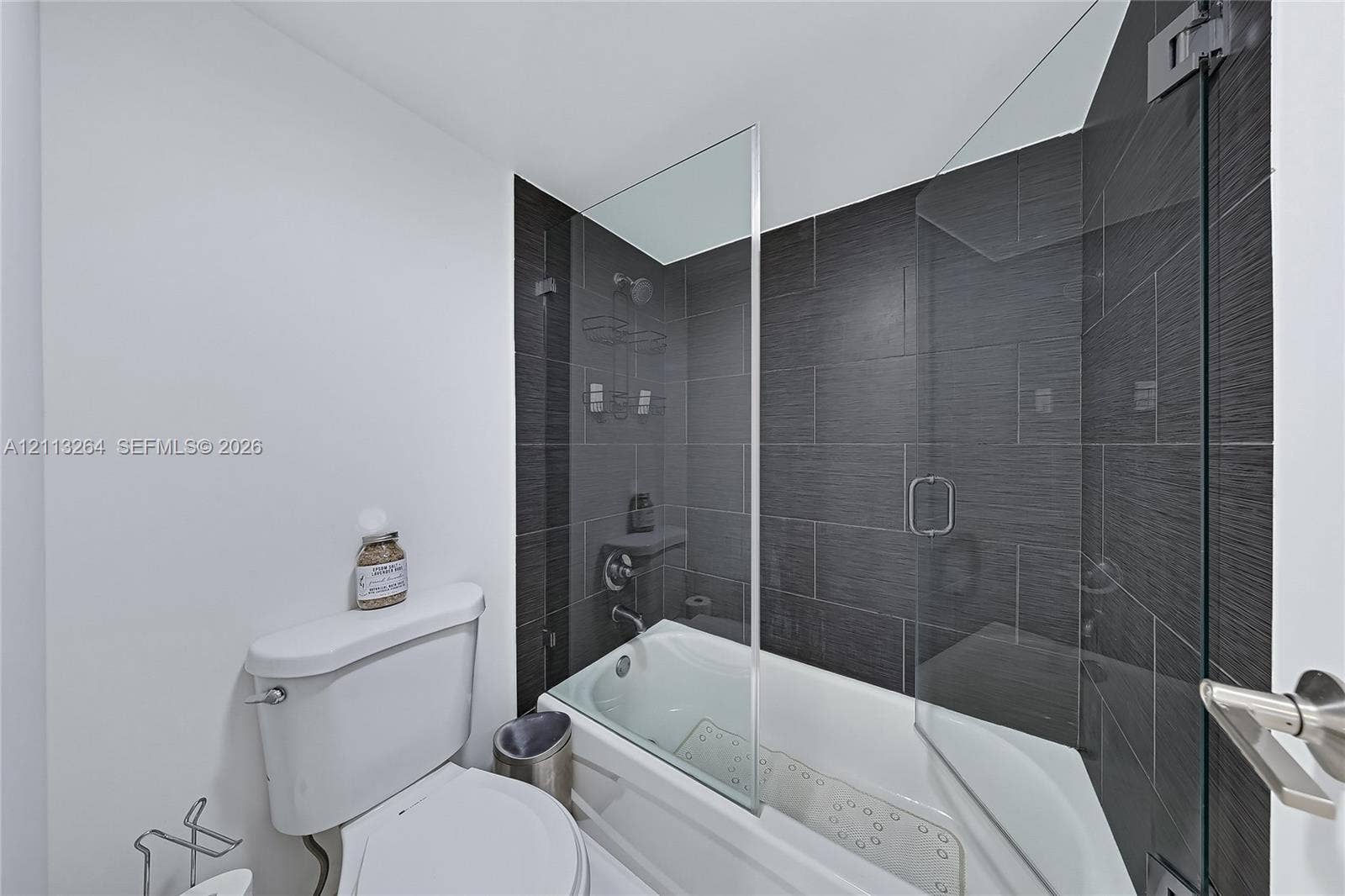 Bathtub featuring a glass shower panel, textured dark wall tiling, and chrome fixtures