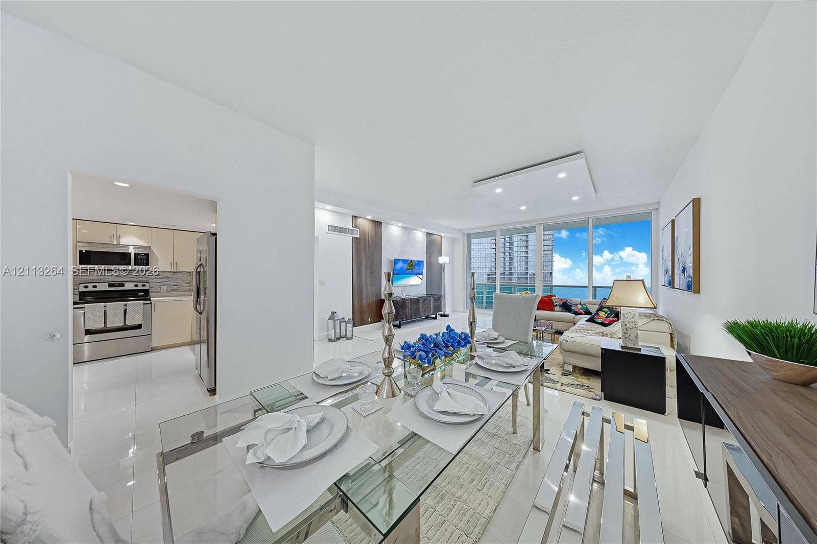Open-concept interior featuring large-format tile flooring, recessed ceiling lighting, full-height windows, and integrated kitchen appliances