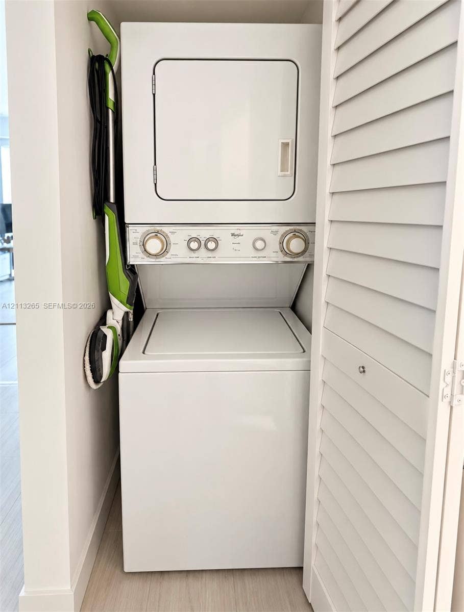 Stackable white laundry unit housed in a closet featuring white louvered doors