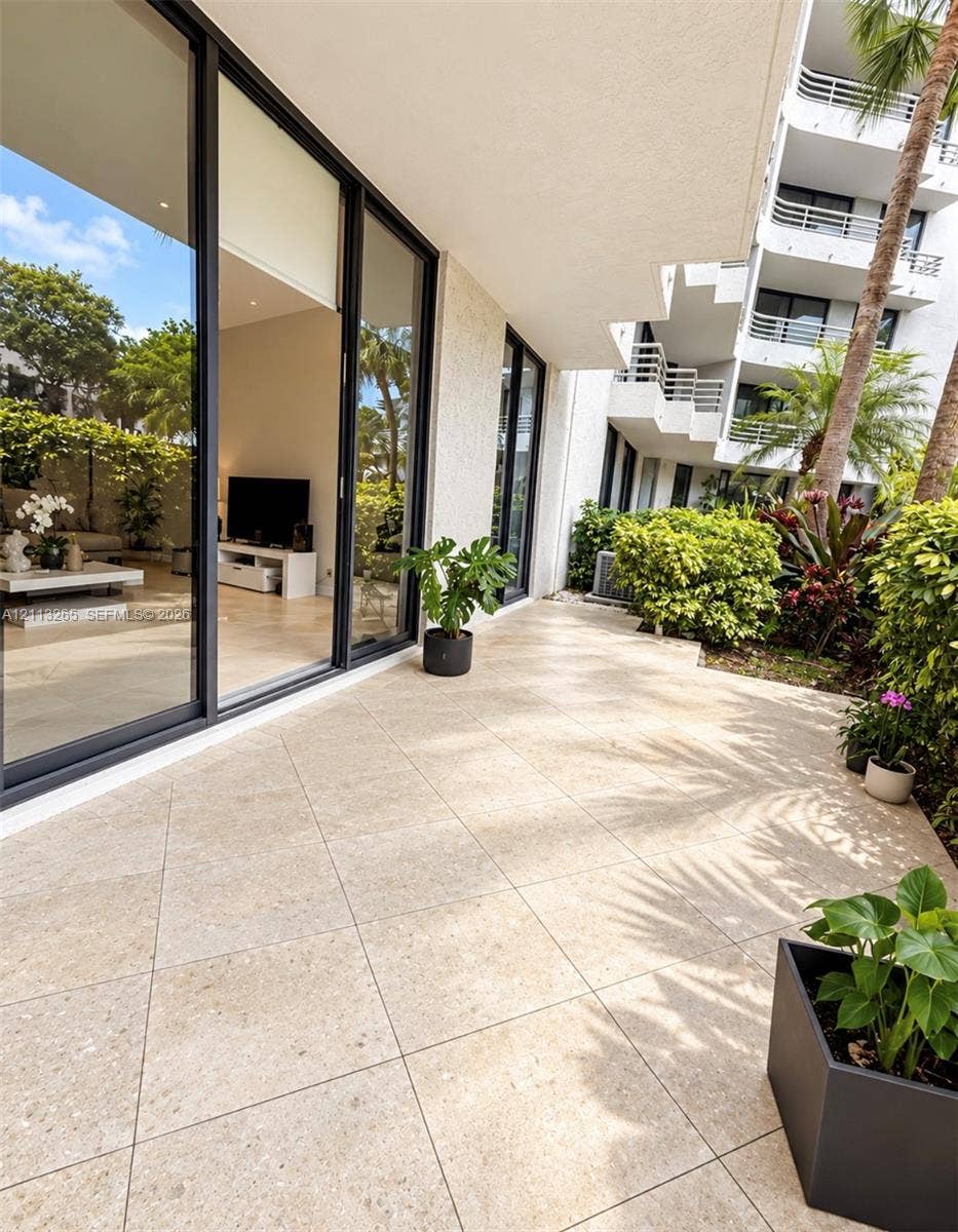 Private patio featuring large-format tile flooring, floor-to-ceiling sliding glass doors with black framing, and stucco exterior finish
