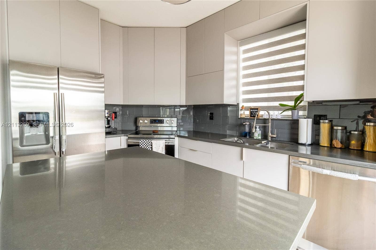 11494 NW 79th Lane, Doral, FL 33178 Contemporary kitchen featuring flat-panel cabinetry, solid-surface countertops, a full-height tile backsplash, and stainless-steel appliances