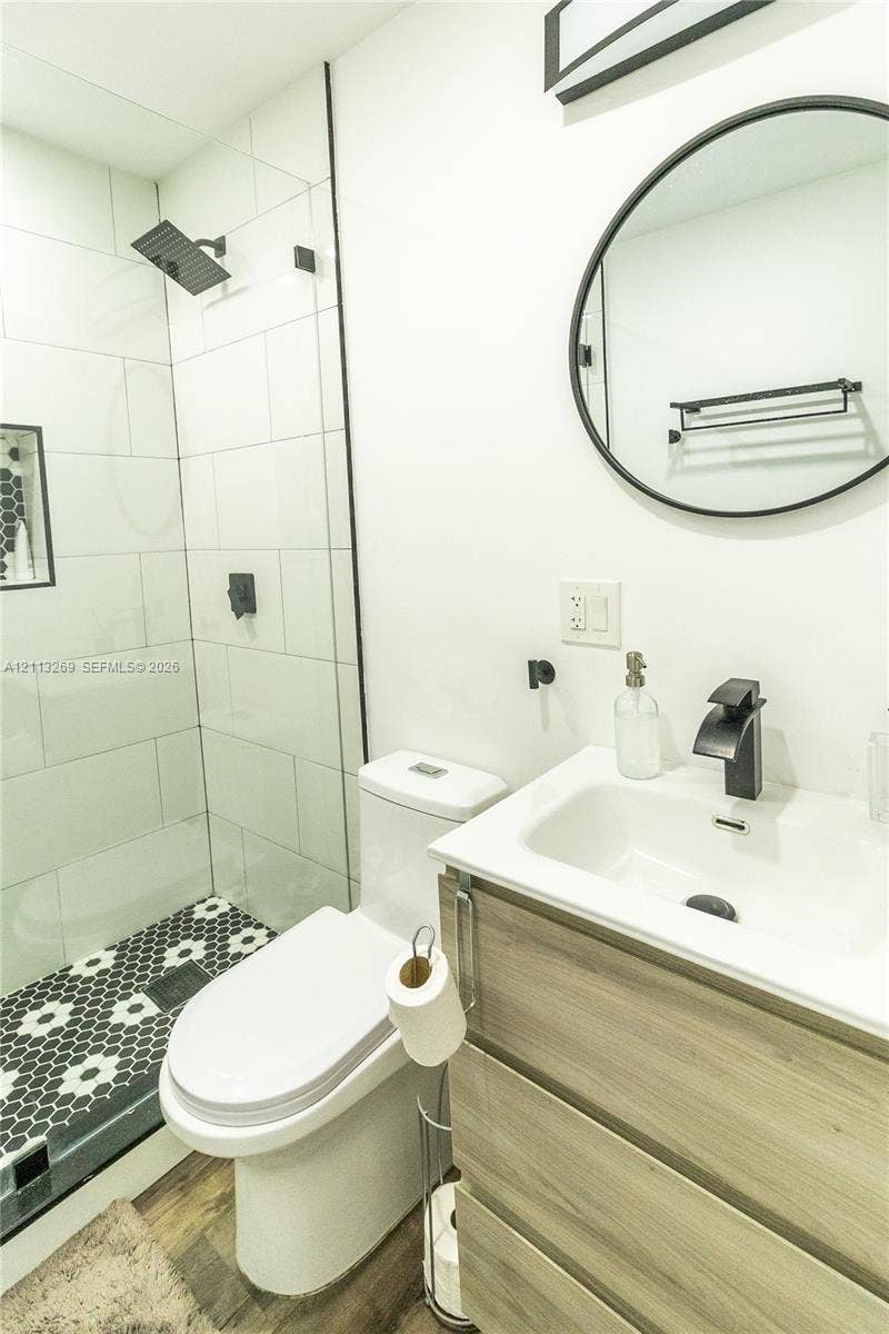11494 NW 79th Lane, Doral, FL 33178 Modern bathroom featuring a wood-finish vanity with a rectangular sink, matte black faucet, frameless glass-enclosed shower with oversized white wall tiles, and hexagonal mosaic floor tiling