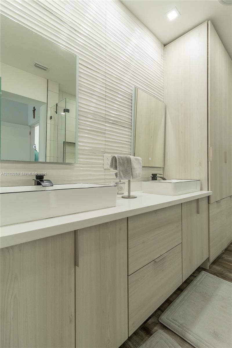11494 NW 79th Lane, Doral, FL 33178 Double vanity featuring wood-finish cabinetry, rectangular vessel sinks, matte black faucets, quartz-style countertops, and textured wall tile