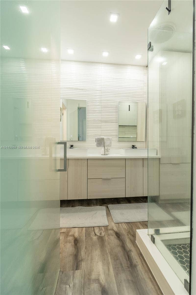 11494 NW 79th Lane, Doral, FL 33178 Dual-sink vanity with light wood-finish cabinetry, quartz countertops, textured tile backsplash, wood-finish flooring, and a glass-enclosed shower