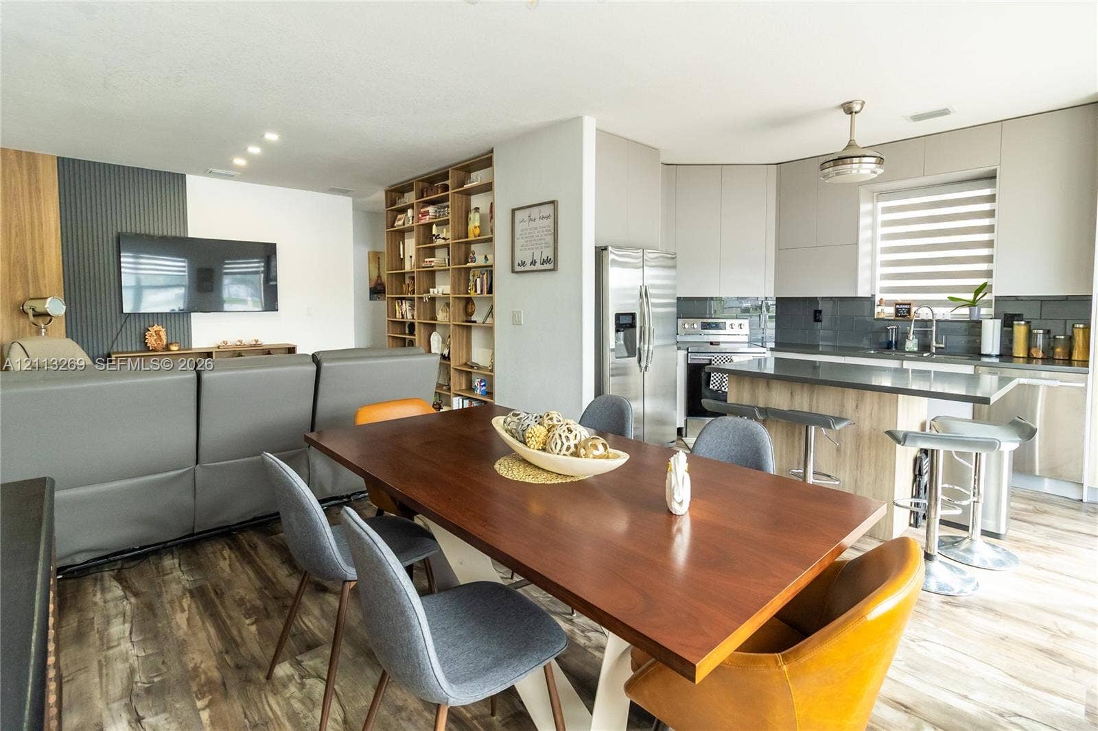 11494 NW 79th Lane, Doral, FL 33178 Kitchen featuring flat-panel cabinetry, a wood-finish island, and stainless steel appliances, accented by floor-to-ceiling built-in shelving and wood-finish flooring