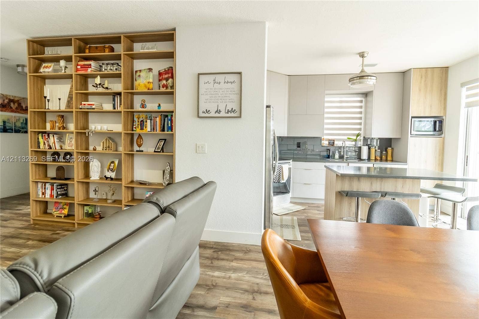 11494 NW 79th Lane, Doral, FL 33178 Custom built-in floor-to-ceiling shelving unit, wood-finish flooring, kitchen island with countertop seating, light grey cabinetry, and horizontal window shades