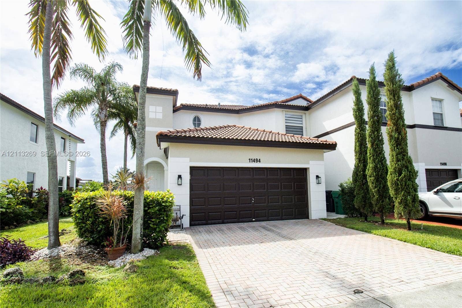 11494 NW 79th Lane, Doral, FL 33178 Stucco exterior featuring a clay tile roof, paved driveway, attached garage, and landscaping
