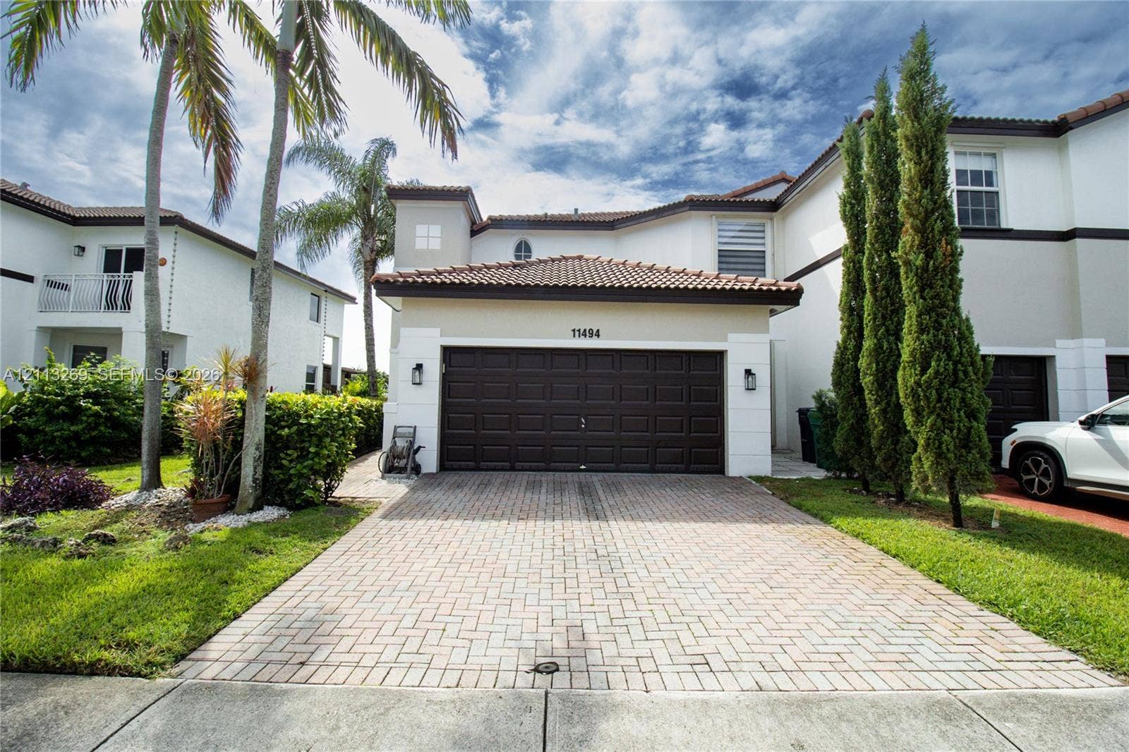 11494 NW 79th Lane, Doral, FL 33178 Stucco exterior featuring a tile roof, paved driveway, dark-toned sectional garage door, and exterior wall-mounted lighting