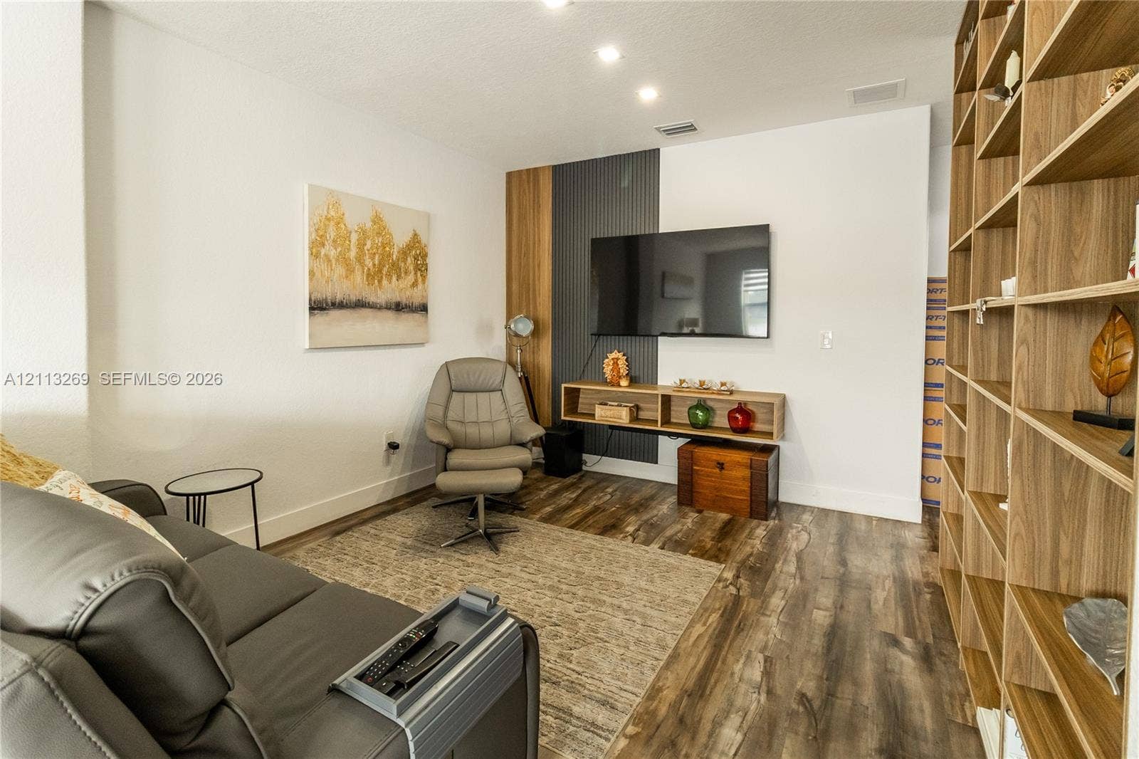 11494 NW 79th Lane, Doral, FL 33178 Custom floor-to-ceiling wood-finish shelving unit, wood-finish flooring, and a dedicated wall feature accented with vertical charcoal paneling and a floating media shelf