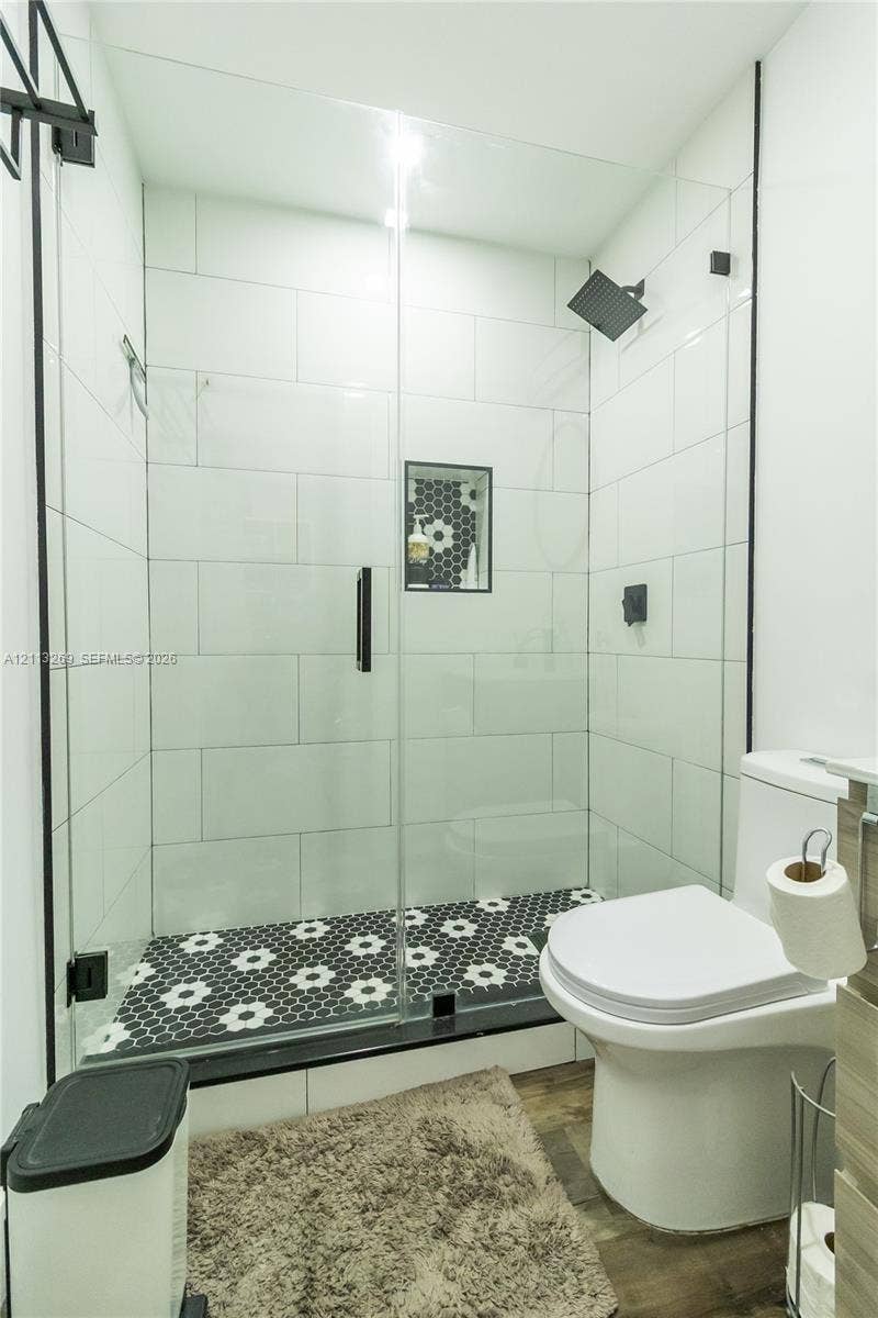 11494 NW 79th Lane, Doral, FL 33178 Walk-in shower with floor-to-ceiling white subway tile, black-and-white patterned tile flooring, built-in shower niche, glass enclosure, and matte black hardware