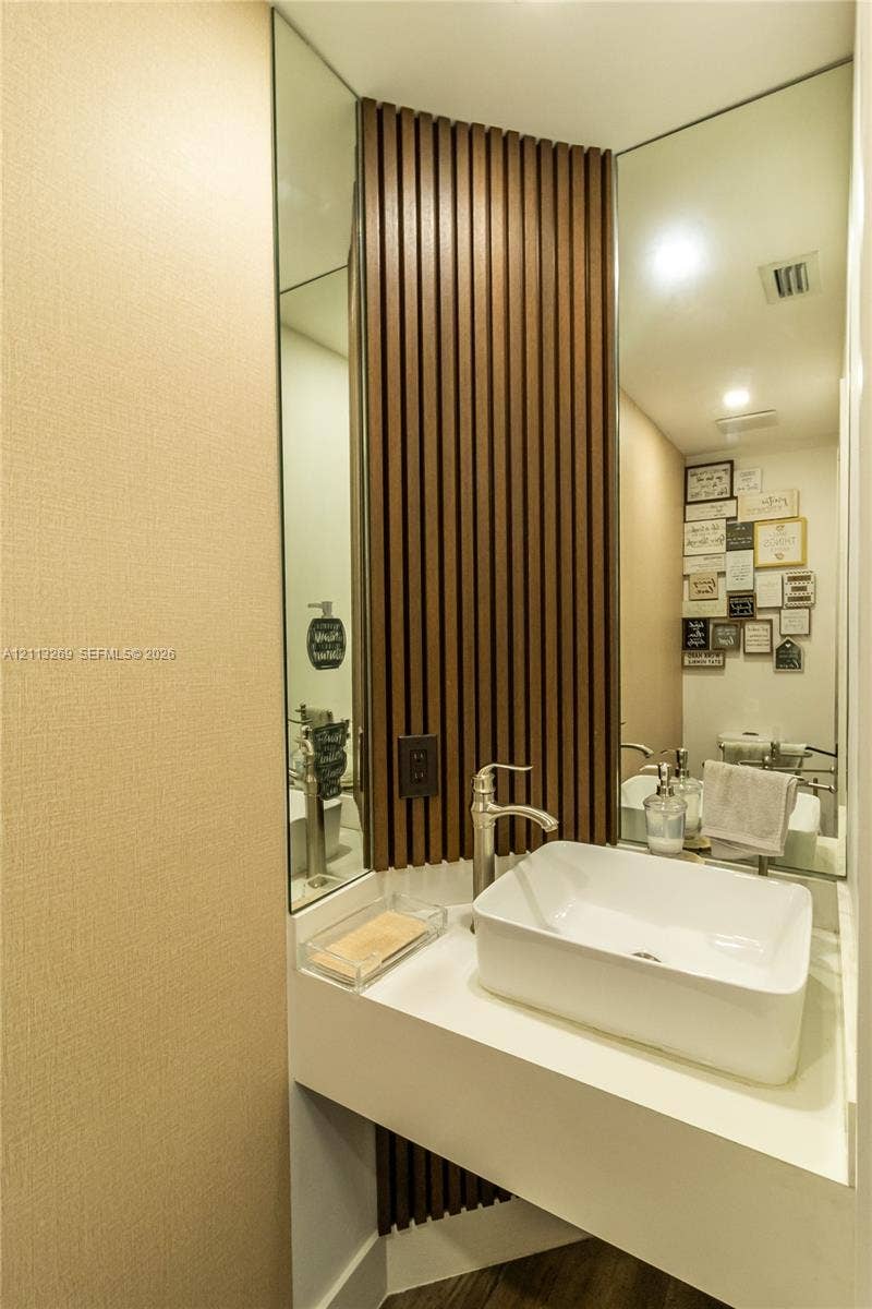 11494 NW 79th Lane, Doral, FL 33178 Wall-mounted vanity featuring a white rectangular vessel sink, metallic faucet, full-height decorative wood slat paneling, and mirrored corner walls