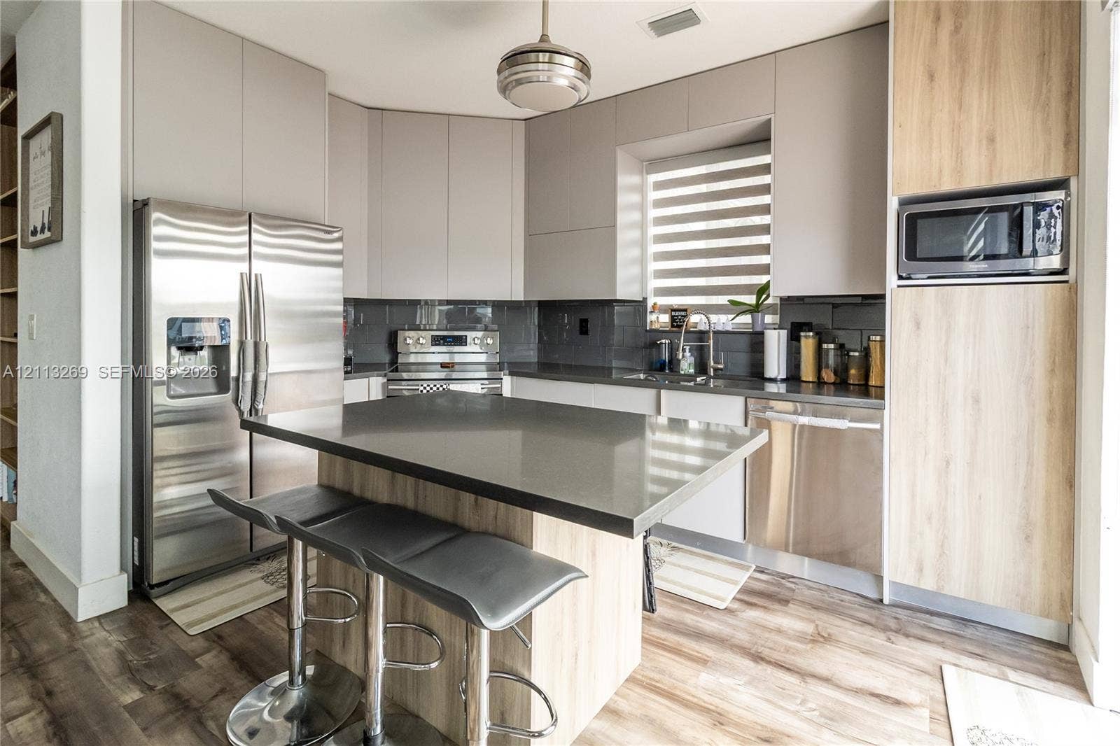 11494 NW 79th Lane, Doral, FL 33178 Modern kitchen featuring sleek flat-panel cabinetry in matte grey and wood-finish, stone-surfaced island, stainless steel appliances, and wood-finish flooring