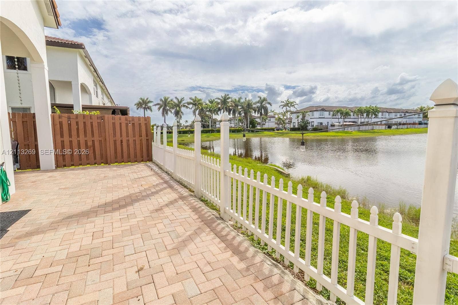 11494 NW 79th Lane, Doral, FL 33178 Paver patio featuring a privacy fence and white picket fencing overlooking a water feature