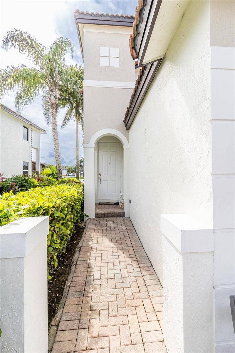 11494 NW 79th Lane, Doral, FL 33178 Exterior entryway featuring a paver stone walkway, arched recessed doorway, and stucco facade with a tile roof accent