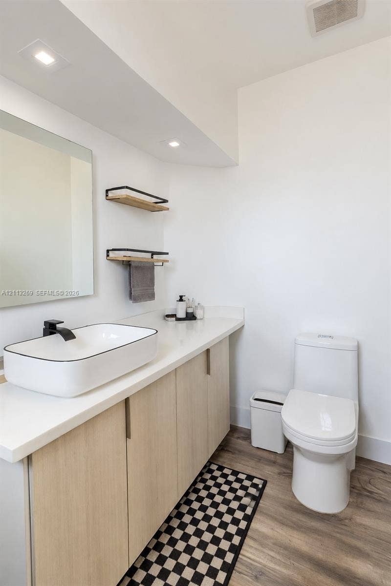 11494 NW 79th Lane, Doral, FL 33178 Light-toned cabinetry with a white countertop, vessel sink, matte black faucet, wall-mounted shelving, and wood-finish flooring