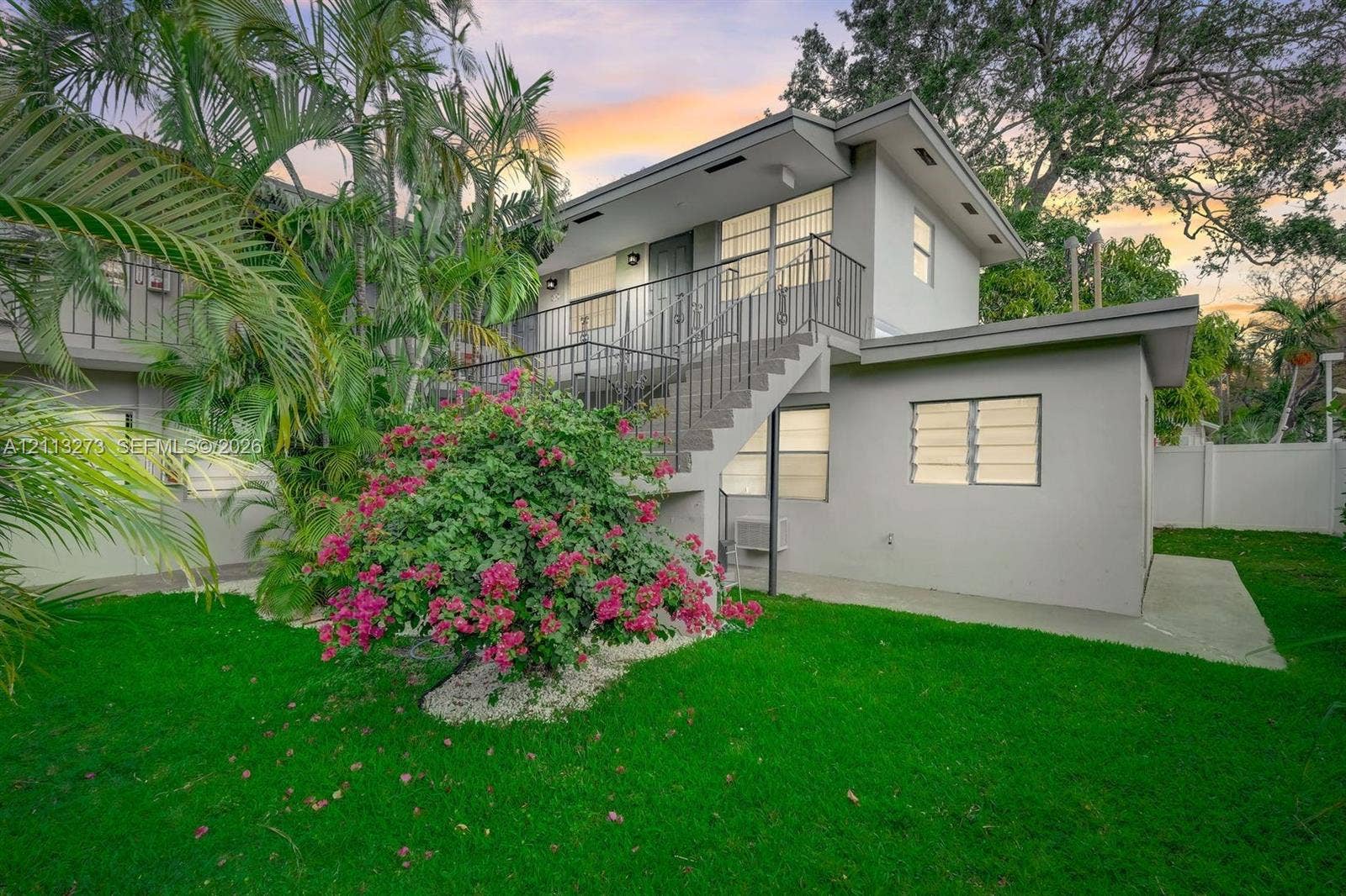 Two-story exterior featuring a metal staircase, railing, louvered windows, and a concrete patio