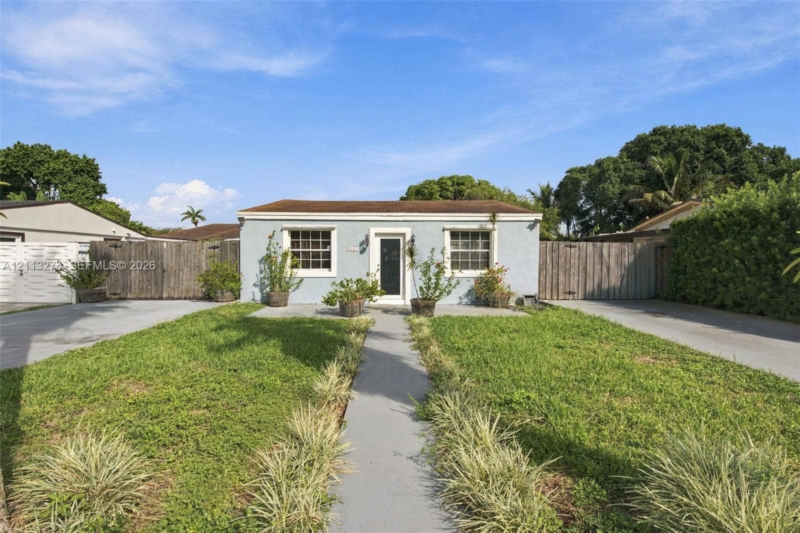 6521 SW 42nd Street, Miami, FL 33155 Single-story residence featuring a light-toned stucco exterior, multi-pane windows, a centered glass-panel front door, and flanking wood-plank fencing