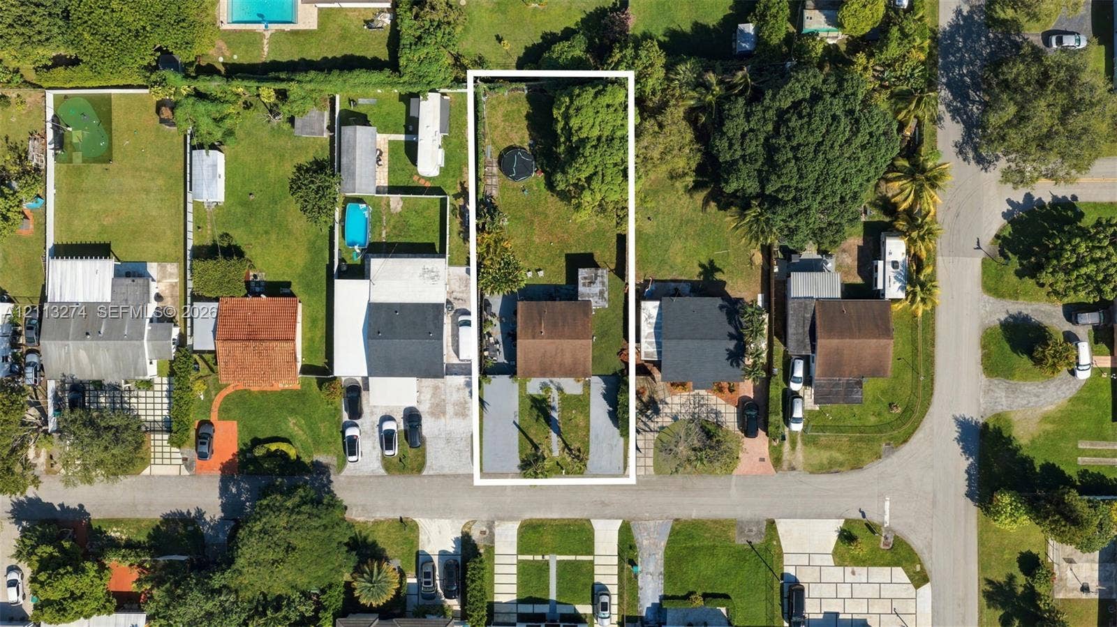 6521 SW 42nd Street, Miami, FL 33155 Aerial perspective of a residential lot featuring a concrete driveway, a central structure with a pitched roof, and an expansive rear yard with mature trees
