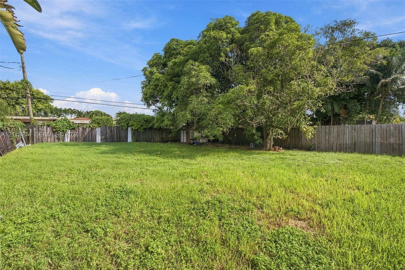 6521 SW 42nd Street, Miami, FL 33155 Expansive backyard featuring a large grass lawn, mature trees, and perimeter wood fencing