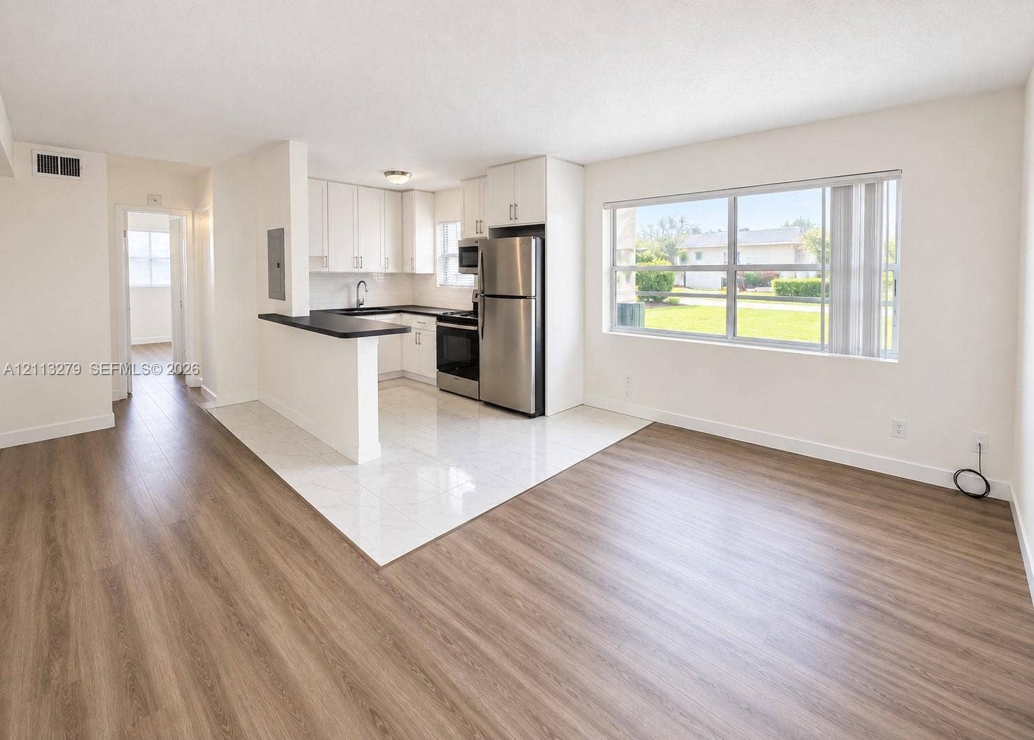 Kitchen featuring white cabinetry, a breakfast bar, and stainless steel appliances, set against wood-finish flooring and ceramic tile
