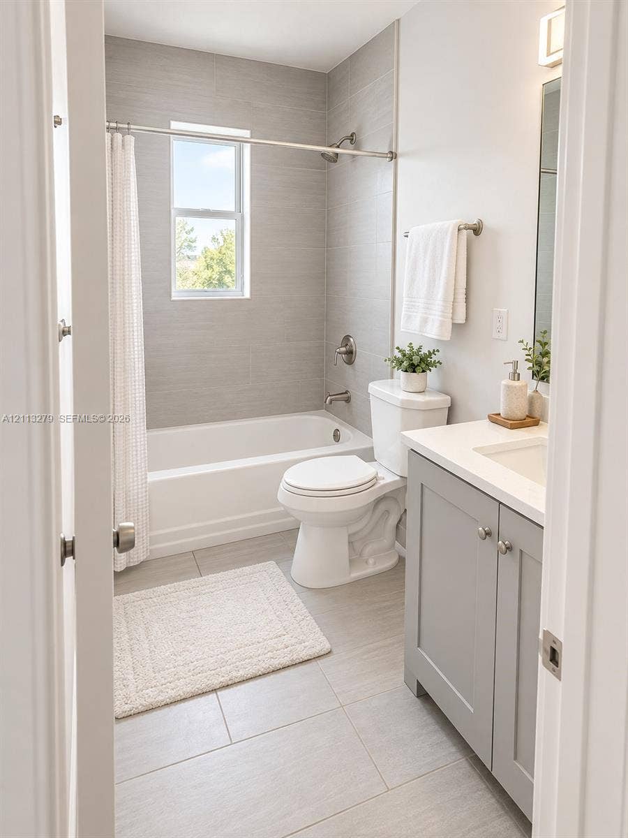 Bathroom featuring a grey vanity with a light-toned countertop, large-format tile flooring, a shower-tub combination with full-height tile surround, and polished nickel fixtures