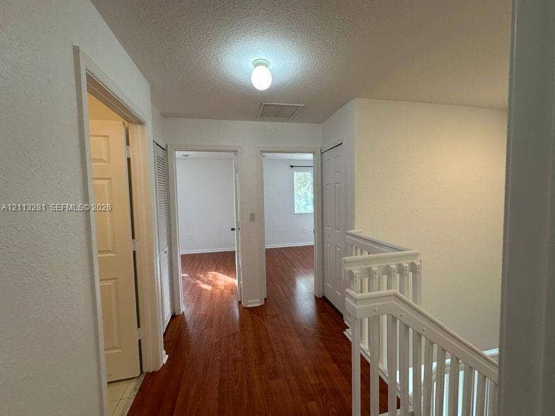 2615 SE 15th Place, #190, Homestead, FL 33035 Hallway featuring wood-finish flooring, white paneled doors, ceiling-mounted light fixture, and wooden staircase railing