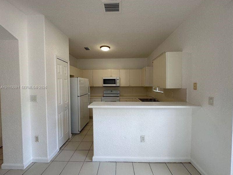 2615 SE 15th Place, #190, Homestead, FL 33035 Kitchen featuring white cabinetry, solid-surface breakfast bar, tile flooring, and built-in appliances